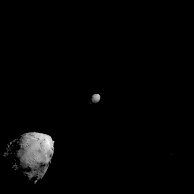 The asteroid Didymos and its small moon Dimorphos, two gray rocky bodies against black space